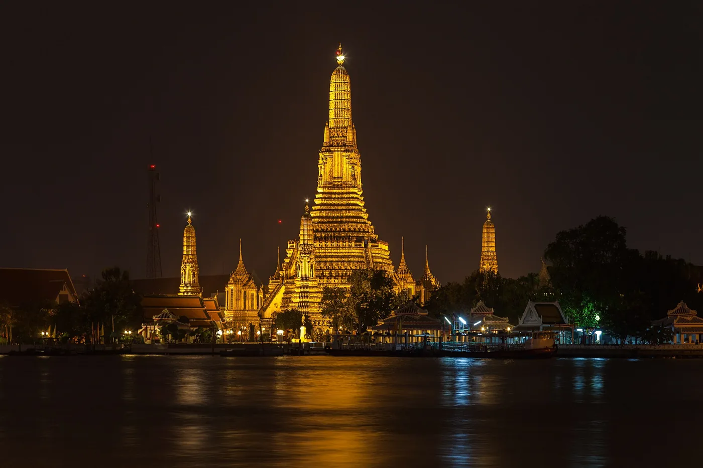 Wat Arun, the Temple of Dawn in Bangkok, lit up at dusk beside the Chao Phraya river.